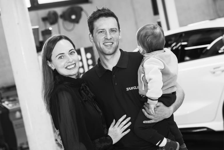 Familie mit Kind steht vor einem Fahrzeug in der Werkstatt